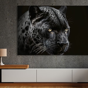 May include: A canvas print featuring a close-up of a black jaguar's face. The jaguar has yellow eyes and a black coat with dark spots. The background is black, emphasizing the animal's features. The artwork is displayed on a wall above a white cabinet.
