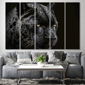 May include: A multi-panel canvas art piece featuring a close-up of a black jaguar with yellow eyes. The jaguar's fur is detailed with spots, and the artwork is set against a dark background. The artwork is displayed above a gray sofa.