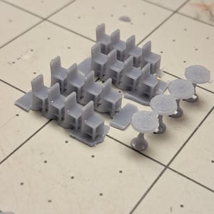 May include: A set of 3D printed miniature chairs and tables. The chairs are gray and have a simple design. The tables are also gray and have a round top.