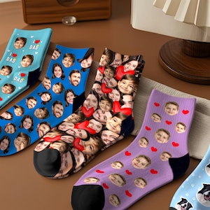 May include: A collection of personalized socks featuring faces and heart designs. The socks are in various colors, including blue, purple, and a multi-colored option. Some socks have "I ❤️ DAD" text.