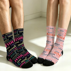 May include: A pair of crew socks featuring the name Jessica printed repeatedly in various fonts and sizes. One sock is black with pink, blue, and white text, while the other is light pink with red, dark pink, and black text, both with black toes.