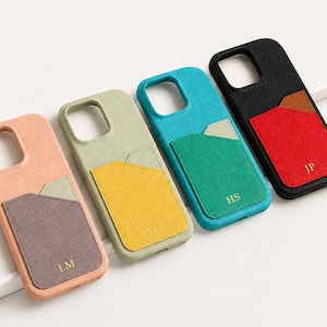 May include: Four smartphone cases with card pockets, arranged in a row. The cases are peach with a grey pocket, light green with a yellow pocket, teal with a green pocket, and black with a red pocket. Each pocket features gold embossed initials.