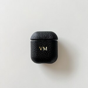 May include: Black leather case for wireless earbuds with the initials "VM" embossed in gold.