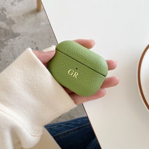 May include: A green leather case for AirPods with the initials "GR" embossed in gold.