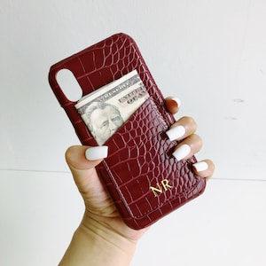 May include: A burgundy faux crocodile leather phone case with a card slot and the initials "NR" in gold lettering.