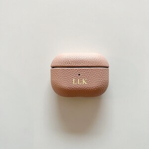 May include: A light pink leather case for wireless earbuds with the initials "LLK" embossed in gold.