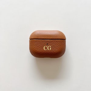 May include: A brown leather case for AirPods with the initials "CG" embossed on the front.