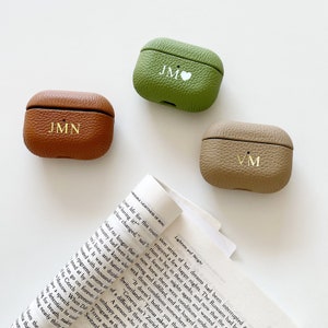 May include: Three leather Airpod cases with personalized initials. The cases are in brown, green, and beige.