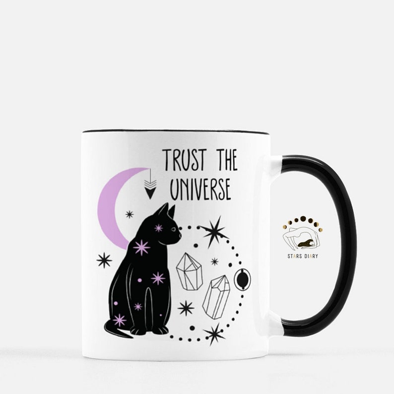 May include: White ceramic mug with a black cat, moon, crystals, and stars design. The mug has a black handle and the text "Trust the Universe" in black. The bottom of the mug has a small logo that says "Stars Diary".