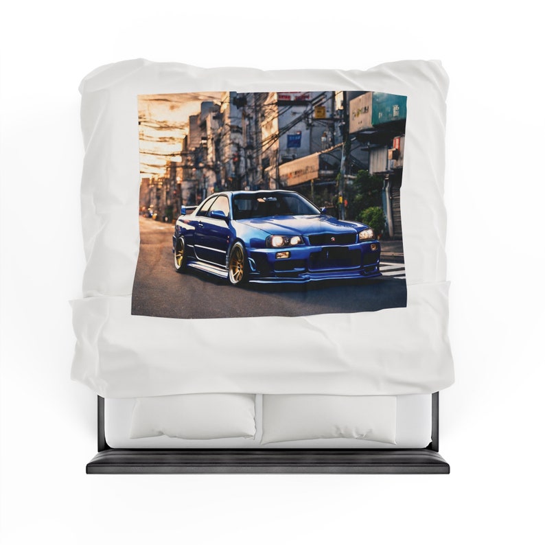 May include: A blue sports car is depicted on a white pillowcase. The car is driving on a city street with buildings in the background. The car has gold rims and a spoiler. The pillowcase is on a black bed frame.