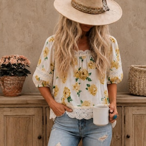 May include: A beige wide-brimmed hat with a decorative band, a white blouse featuring a yellow floral pattern and lace trim, and light blue distressed denim jeans. The blouse has three-quarter length sleeves and a scalloped lace hemline.