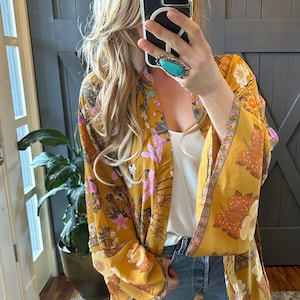 May include: A long, yellow floral kimono with pink and brown accents. The kimono has a wide, flowing silhouette and a tie closure at the waist.