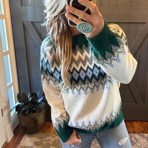 Può includere: Maglione color crema con un motivo geometrico verde, blu e grigio. Il maglione ha polsini e orlo verdi. Il design presenta un motivo a zig-zag nelle tonalità del blu, grigio e crema.