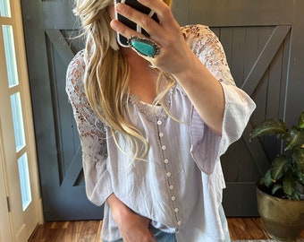 May include: A light purple blouse with a lace trim on the sleeves and a button-up front. The blouse is worn with blue jeans.