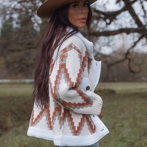 May include: A cream-coloured jacket with a brown and white geometric pattern. The jacket has a white collar and cuffs. A brown hat is also visible.