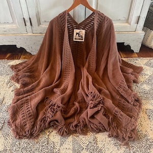 Könnte beinhalten: Ein braunes gestricktes Tuch mit Fransen. Das Tuch hat ein gehäkeltes Muster und ist aus einem weichen, gemütlichen Material gefertigt.