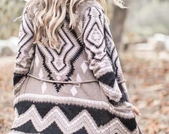 May include: A long-sleeved cardigan with a geometric pattern in shades of brown, black, and white. The cardigan has a tie belt and a relaxed fit.