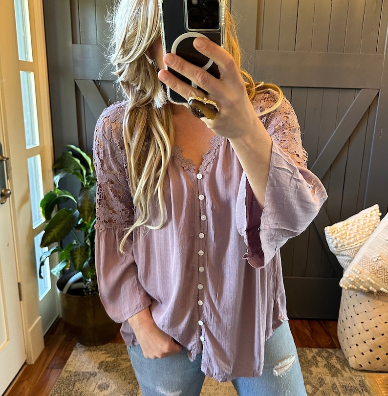 May include: A mauve button-up blouse with lace detailing on the sleeves. The blouse has a relaxed fit and is made of a lightweight fabric.