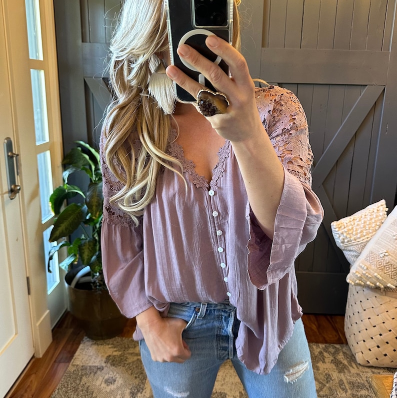 May include: A mauve button-down blouse with lace detailing on the sleeves. The blouse is loose-fitting and has a V-neckline.