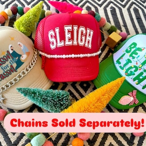 May include: Three Christmas themed trucker hats. The first hat is beige with a white design that says "Reason for the Season" and a silver chain. The second hat is red with a white design that says "SLEIGH". The third hat is green with a white design that says "Be the Light" with a string of white lights. The text "Chains Sold Separately!" is at the bottom of the image.