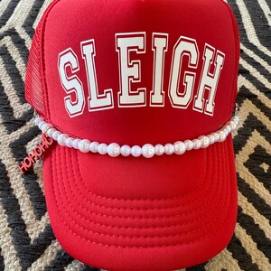 May include: Red trucker hat with a white "SLEIGH" logo and a pearl necklace trim. The hat has a black mesh back.