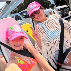 Op de afbeelding: Twee mensen dragen roze en witte hoeden met het woord "30A" erop. De persoon vooraan draagt een roze en oranje bikini top en een zwarte harnas. De persoon achteraan draagt een wit gehaakt top met een blauwe en witte bikini top eronder.