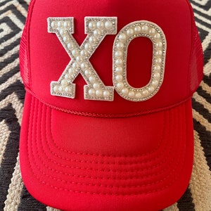 May include: Red trucker hat with a white "XO" design made of pearls and rhinestones.