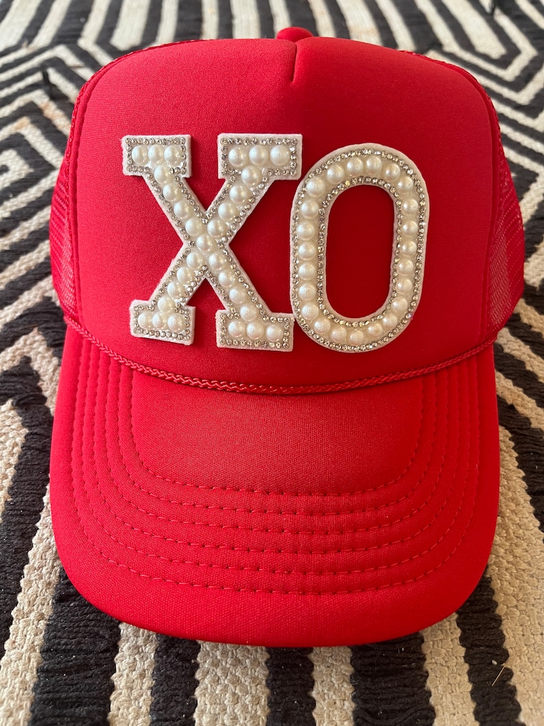 May include: Red trucker hat with a white "XO" design made of pearls and rhinestones.