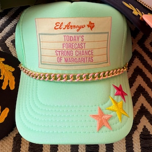 May include: A mint green trucker hat with a gold and pink chain detail on the brim. The hat features embroidered stars and the text "El Arroyo Today's Forecast Strong Chance of Margaritas."