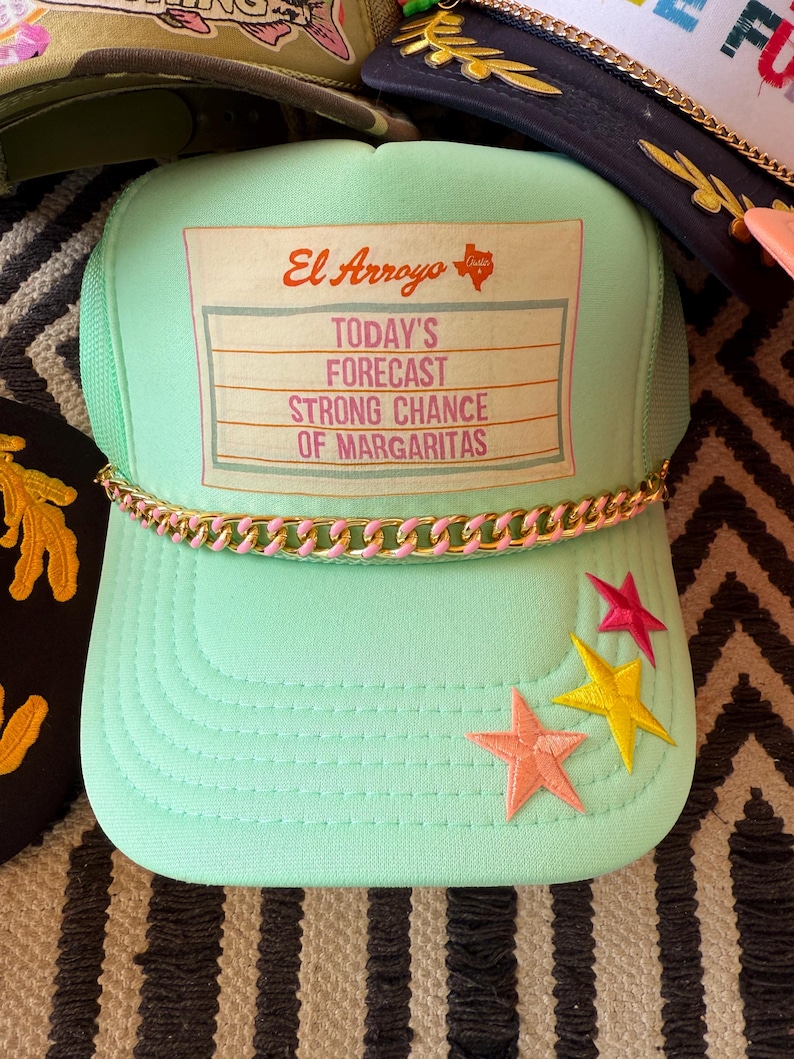 May include: A mint green trucker hat with a gold and pink chain detail on the brim. The hat features embroidered stars and the text "El Arroyo Today's Forecast Strong Chance of Margaritas."