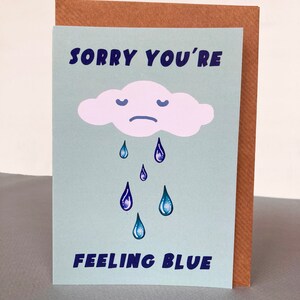 May include: A light blue card with a white cloud with a sad face and blue raindrops. The card says "Sorry you're feeling blue".