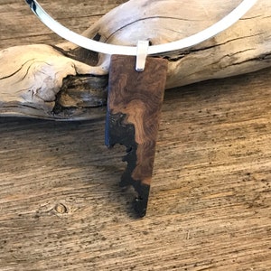 May include: A silver necklace with a wooden pendant. The pendant is dark brown with black accents and has a unique, irregular shape.