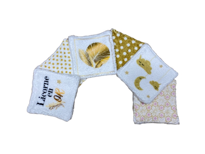Puede incluir: Seis almohadillas de algod&oacute;n blanco para desmaquillar con diferentes dise&ntilde;os bordados en dorado. Los dise&ntilde;os incluyen una hoja de palma dorada, lunares dorados, una luna y estrellas doradas, y el texto "Licorne en Or".