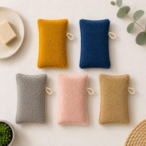 Può includere: Cinque spugne rettangolari con una superficie ruvida e soffice, ciascuna dotata di un piccolo occhiello laterale. Le spugne sono di colore giallo senape, blu navy, grigio, rosa chiaro e marrone chiaro, disposte su una superficie neutra.