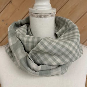 Pode incluir: Um cachecol verde claro e branco em vichy com um padrão xadrez. O cachecol está dobrado e exposto em um manequim branco.