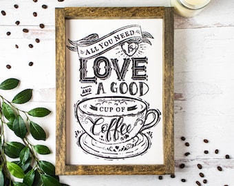 May include: A framed black and white sign with the text "All you need is love and a good cup of coffee". The sign features a stylized illustration of a coffee cup and saucer.