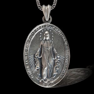 Puede incluir: Pendiente ovalado de plata con una representación de la Virgen María y el texto "O Marie conçue sans péché priez pour nous qui avons recours à vous" y "1830".
