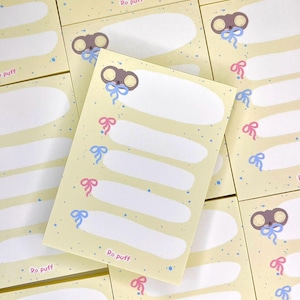 以下が含まれることがあります： 漫画のネズミのデザインが施された黄色のメモ帳の束。各メモ帳には書き込みスペースと「Po puff」というテキストが印刷されています。