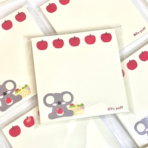 以下が含まれることがあります： 赤いリンゴの縁取りがされた、かわいいコアラをテーマにした付箋のセット。各付箋には、赤いリンゴとピクニックバスケットを持った灰色のコアラが描かれています。付箋は透明なプラスチックに包まれており、「@Po puff」という文字が印刷されています。