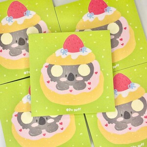以下が含まれることがあります： イチゴをトッピングしたクリーム色のペストリーをかぶった、漫画のオウムのイラストが描かれた緑色の正方形のカードが5枚。ペストリーはピンク色のフロスティングとハートで飾られています。各カードには「@Po puff」の文字が書かれています。