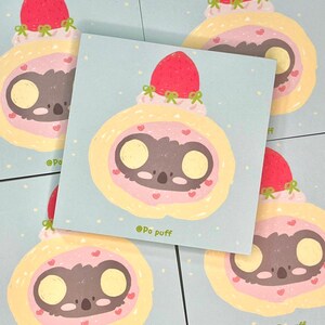 以下が含まれることがあります： パステルブルーの正方形のカード5枚セット。ピンクとイエローの渦巻きケーキの中に、赤いイチゴを乗せたコアラの顔の漫画イラストが描かれています。各カードの下部には「@Po puff」の文字があります。