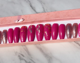 May include: A set of 10 pink coffin-shaped press-on nails with gold glitter accents. Some nails have a gold foil design.