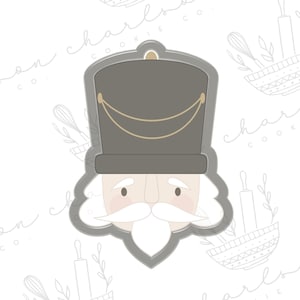 Könnte beinhalten: Ein grauer Ausstecher in Form eines Nussknackerkopfes. Der Ausstecher hat einen schwarzen Hut mit goldener Verzierung und einen weißen Bart.