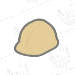 May include: A cookie cutter in the shape of a hard hat. The cutter is made of metal and has a gray finish. The hard hat is yellow and has a black brim.