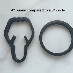 May include: A black 4-inch bunny cookie cutter compared to a 3-inch circle cookie cutter. Both cutters are made of black plastic.