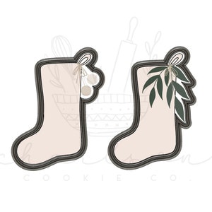 May include: Two black cookie cutters shaped like Christmas stockings with a white outline. One stocking has a green leafy sprig with a white bow and three white ornaments. The other stocking has a green leafy sprig with a white bow.