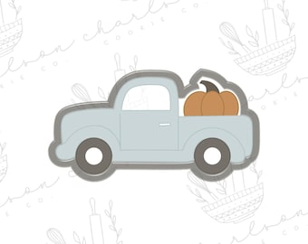 May include: A light blue cookie cutter shaped like a pickup truck with a pumpkin in the bed. The truck has a rounded cab and a flatbed.