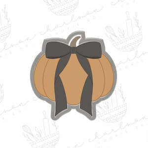 May include: A brown pumpkin cookie cutter with a black bow. The cookie cutter is a simple design with a rounded shape and a stem.