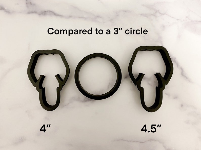 May include: Three cookie cutters, one round and two shaped like a person's head, are shown on a white marble surface. The round cutter is 3 inches in diameter. The head-shaped cutters are 4 inches and 4.5 inches tall. The text "Compared to a 3" circle" is above the cutters.