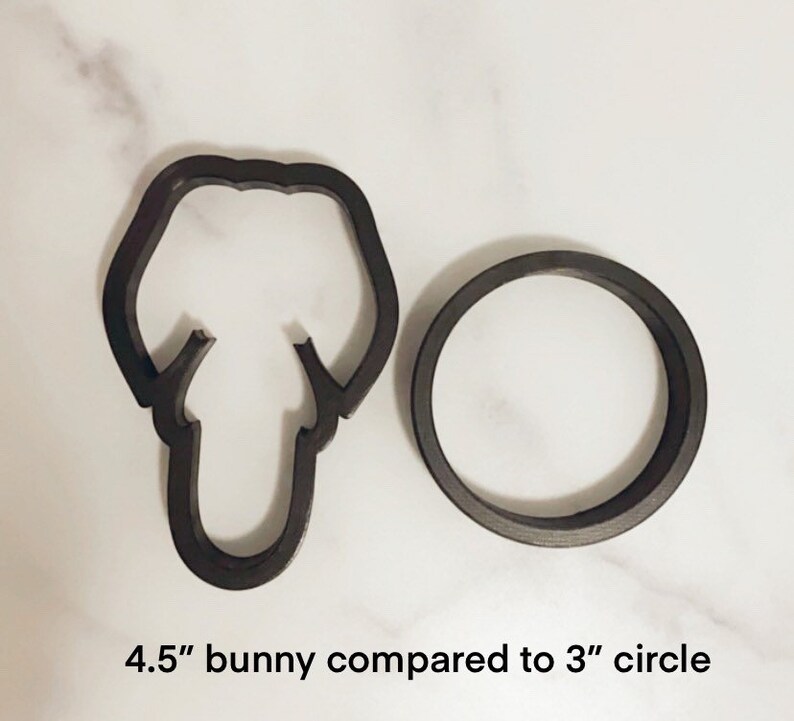 May include: A black 4.5 inch bunny cookie cutter next to a 3 inch black circle cookie cutter. The cookie cutters are on a white surface.